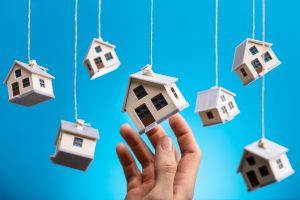 Person's Hand Holding Hanging Model House Against Blue Background