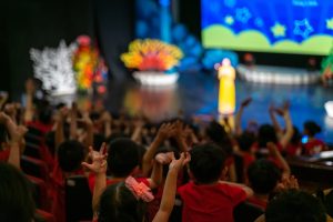Children excitingly raise hands watching the performance in the theater